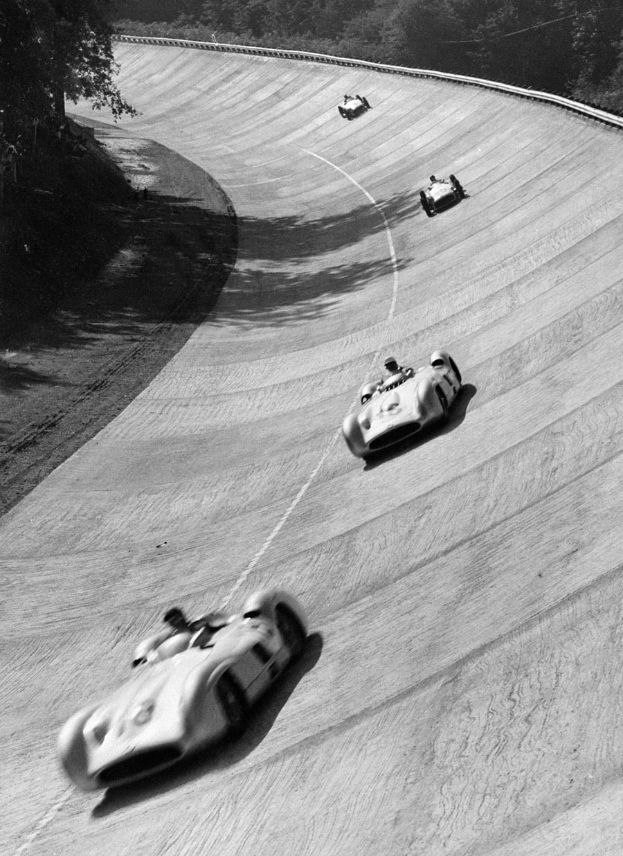 The streamline Mercedes of Juan Manuel Fangio and Stirling Moss lead the field through the banking 