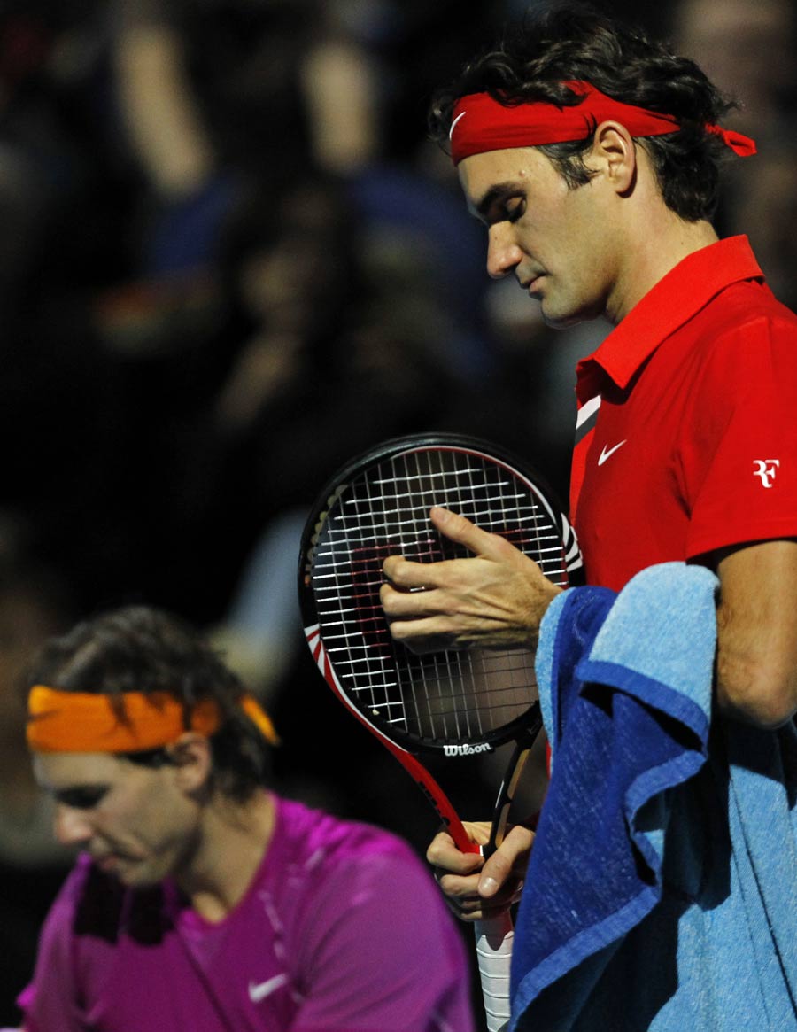 Roger Federer adjusts his racket while Rafael Nadal looks on