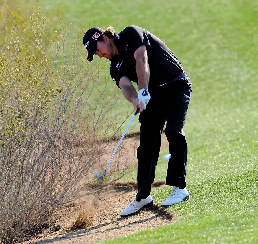 Graeme McDowell hits a shot after taking a drop on the first hole