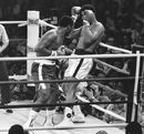 Muhammad Ali peeks through his raised gloves as Joe Frazier backs the champion against the ropes