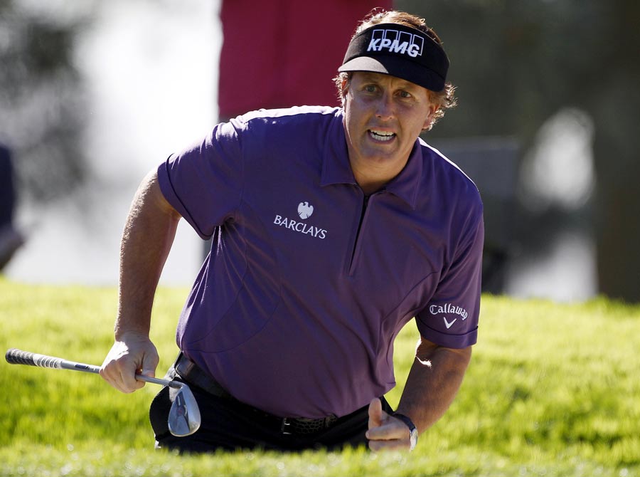 Phil Mickelson stands in the bunker as watches his shot on the green of the first hole
