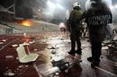Greek riot police walk close to debris