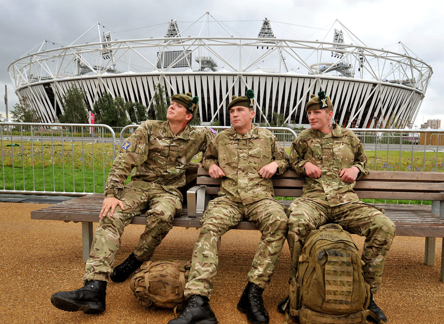 A group of three soldiers from the Royal Regiment of Scotland rest in front of the Olympic Stadium