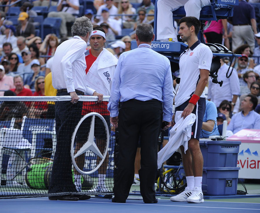 Novak Djokovic and David Ferrer talk to officials as play is suspended
