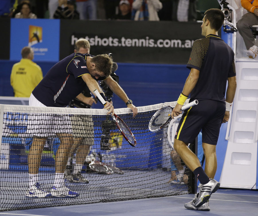 Stanislas Wawrinka slumps over the net as Novak Djokovic moves to shake hands