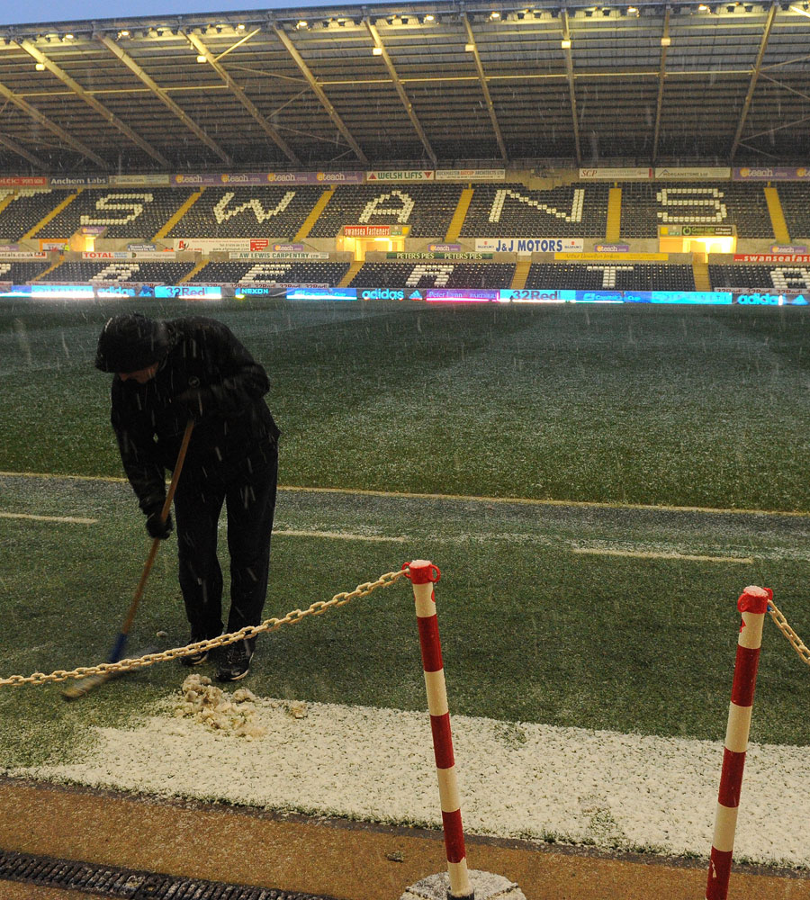 A member of the ground staff sweeps snow from the sides of the pitch