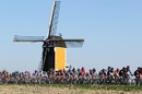 Cyclists stream past a windmill