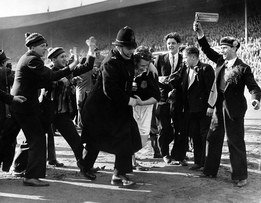 Scotland captain George Young is rushed off the pitch by a policeman to avoid the enthusiastic congratulations of his country's fans after their team won 3-1